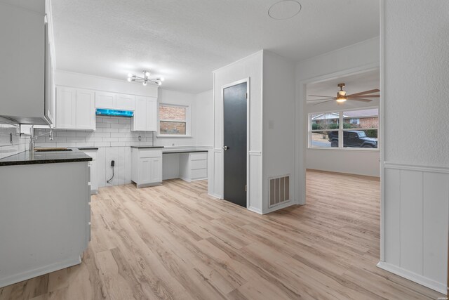 kitchen with tasteful backsplash, visible vents, white cabinets, dark countertops, and light wood-style flooring