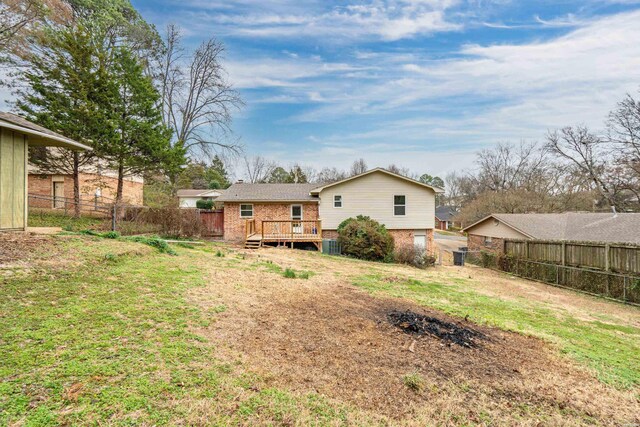 rear view of property featuring brick siding, a fenced backyard, a lawn, and a wooden deck