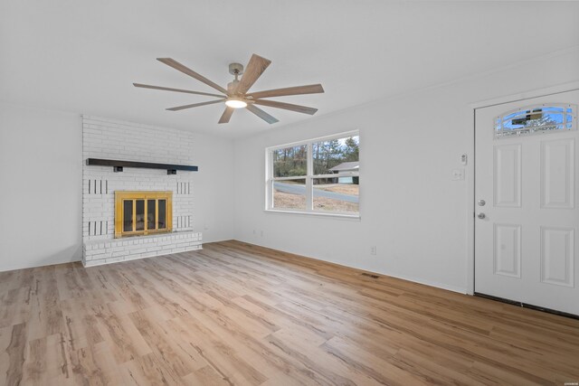 unfurnished living room with a brick fireplace, ceiling fan, and light wood-style flooring