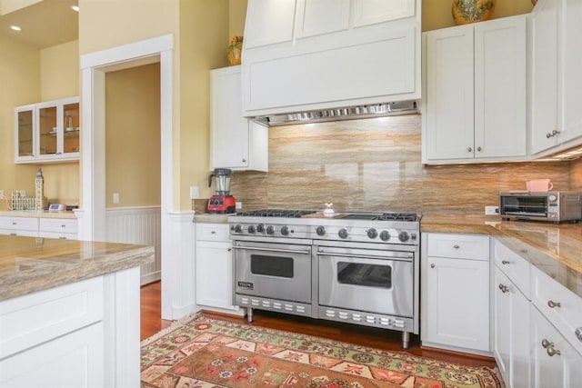 kitchen featuring light stone counters, white cabinets, double oven range, and glass insert cabinets