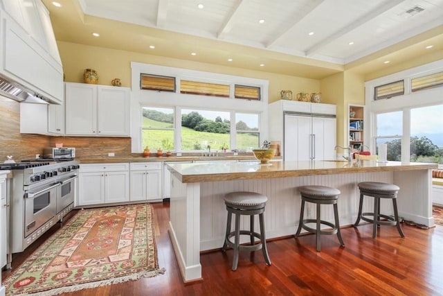 kitchen with high end appliances, custom range hood, a kitchen island, a breakfast bar, and white cabinetry