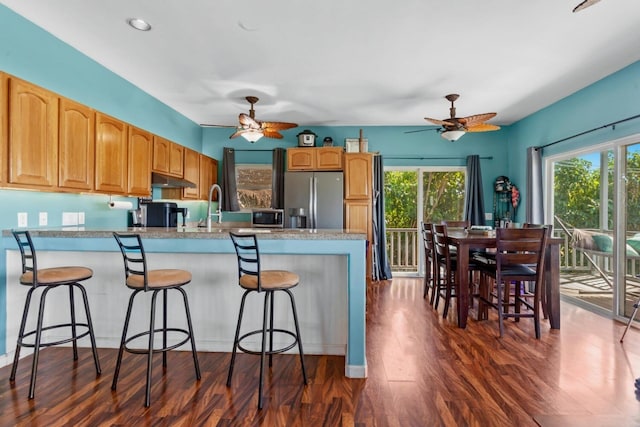 kitchen with a kitchen breakfast bar, ceiling fan, dark hardwood / wood-style floors, and stainless steel refrigerator with ice dispenser