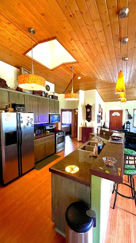 kitchen with a kitchen breakfast bar, appliances with stainless steel finishes, wood ceiling, and light wood-type flooring