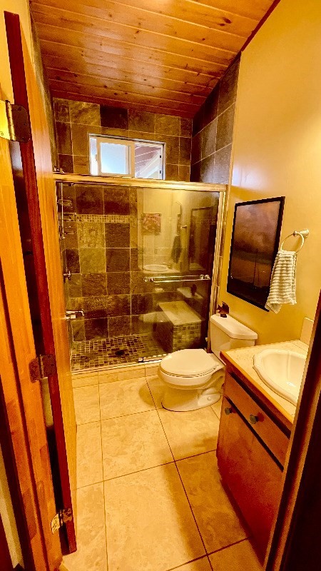 bathroom with toilet, a shower with door, vanity, wood ceiling, and tile floors