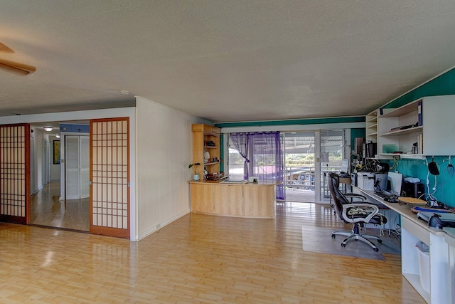 home office featuring light wood-type flooring, ceiling fan, and a textured ceiling