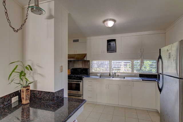 kitchen featuring stainless steel appliances, wall chimney range hood, light tile flooring, white cabinetry, and sink