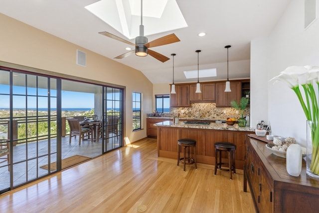 kitchen featuring backsplash, light wood-type flooring, pendant lighting, ceiling fan, and a kitchen breakfast bar