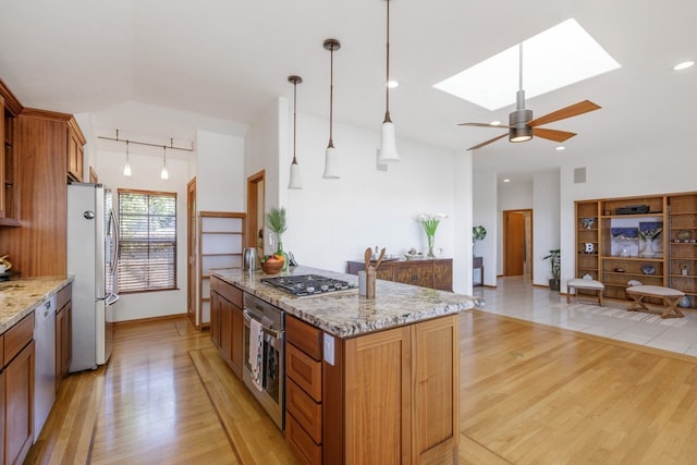 kitchen with light stone countertops, ceiling fan, light hardwood / wood-style flooring, stainless steel appliances, and a center island with sink