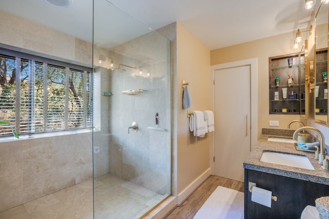 bathroom with dual sinks, a shower with door, wood-type flooring, and vanity with extensive cabinet space