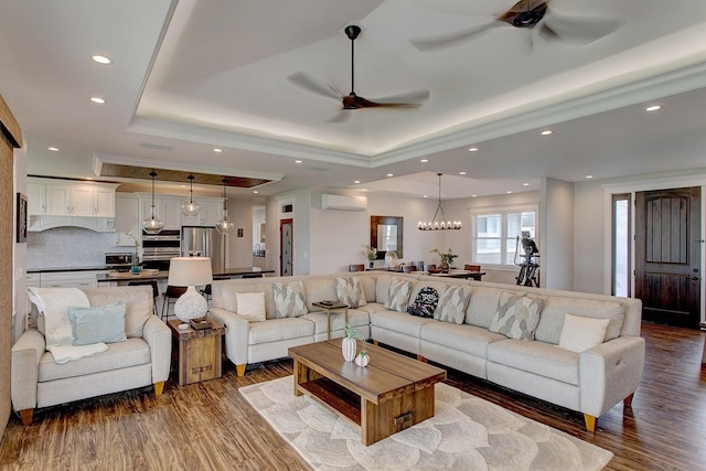 living room featuring a raised ceiling, ceiling fan with notable chandelier, a wall mounted air conditioner, and wood-type flooring