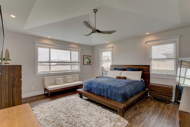 bedroom featuring a tray ceiling, multiple windows, dark hardwood / wood-style floors, and ceiling fan