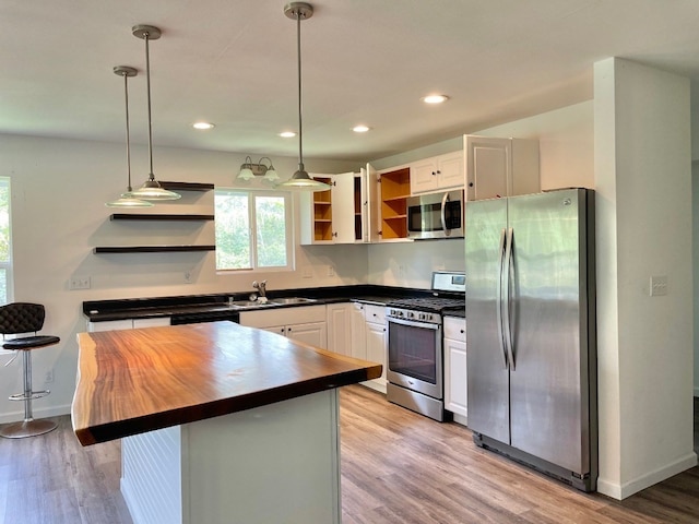 kitchen with appliances with stainless steel finishes, light hardwood / wood-style floors, decorative light fixtures, sink, and white cabinets