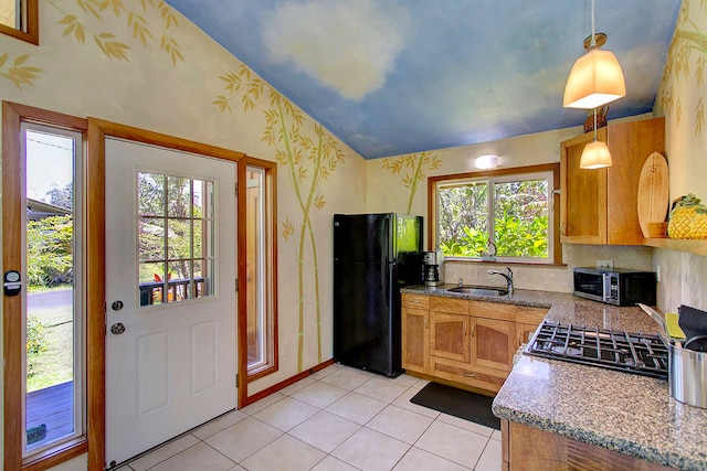 kitchen with pendant lighting, light tile floors, light stone countertops, vaulted ceiling, and black refrigerator