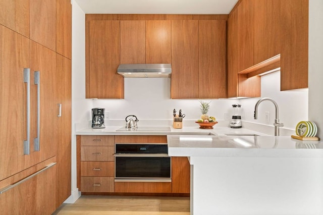 kitchen featuring light stone counters, light hardwood / wood-style floors, black electric cooktop, sink, and oven