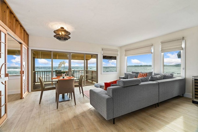 living room with wine cooler, a water view, and light hardwood / wood-style flooring