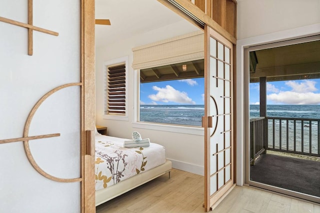 bedroom featuring a water view, access to outside, and light hardwood / wood-style flooring