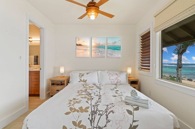 bedroom featuring light hardwood / wood-style floors, ensuite bath, ceiling fan, and a water view