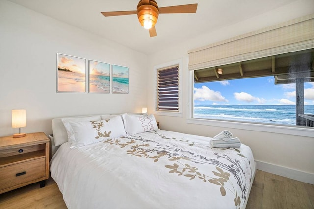 bedroom with light hardwood / wood-style flooring, ceiling fan, and a water view