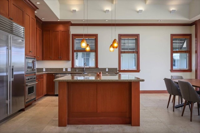 kitchen with light stone countertops, pendant lighting, sink, and built in appliances