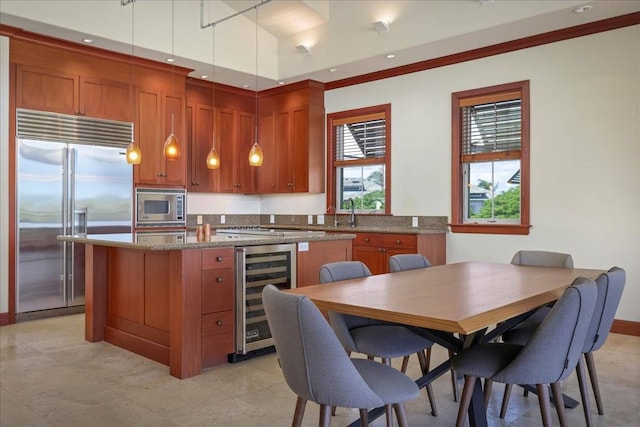 kitchen featuring hanging light fixtures, built in appliances, wine cooler, and light stone counters