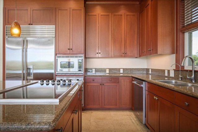 kitchen with pendant lighting, dark stone counters, built in appliances, and sink