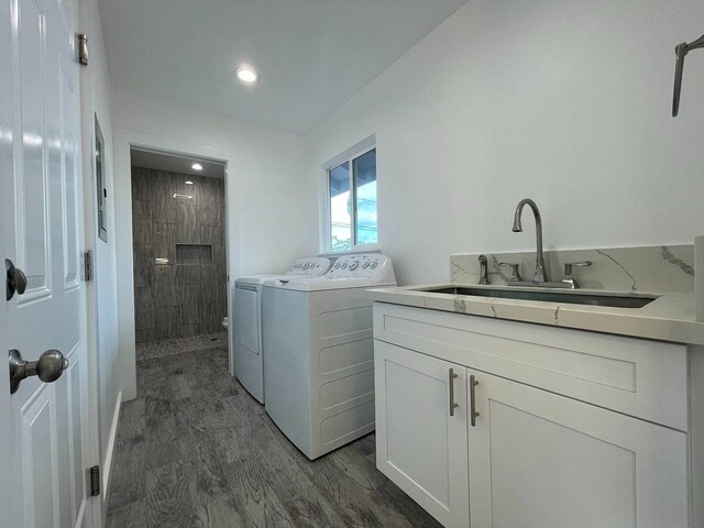 clothes washing area with washing machine and clothes dryer, sink, cabinets, and dark hardwood / wood-style flooring