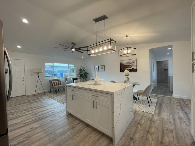 kitchen with light stone counters, ceiling fan with notable chandelier, white cabinetry, and light wood-type flooring