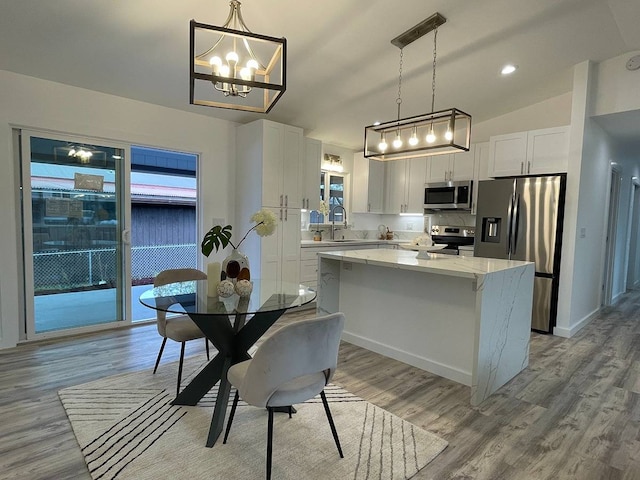 kitchen with appliances with stainless steel finishes, a kitchen island, decorative light fixtures, and white cabinets