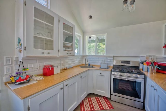 kitchen with sink, stainless steel gas range oven, white cabinets, vaulted ceiling, and tasteful backsplash