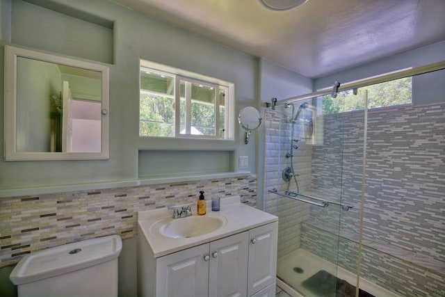 bathroom featuring tile walls, toilet, vanity with extensive cabinet space, a shower with door, and backsplash