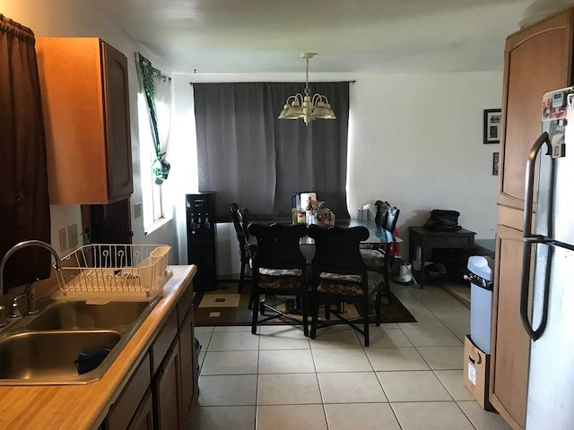 kitchen featuring pendant lighting, a notable chandelier, light tile flooring, stainless steel fridge, and sink