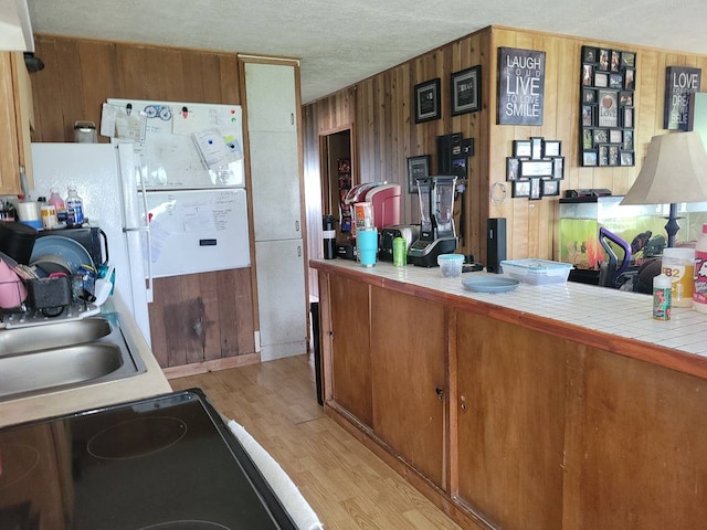 kitchen featuring tile counters, stove, light wood-type flooring, a textured ceiling, and sink