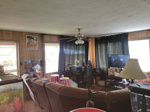 living room with ceiling fan, wood walls, and a textured ceiling