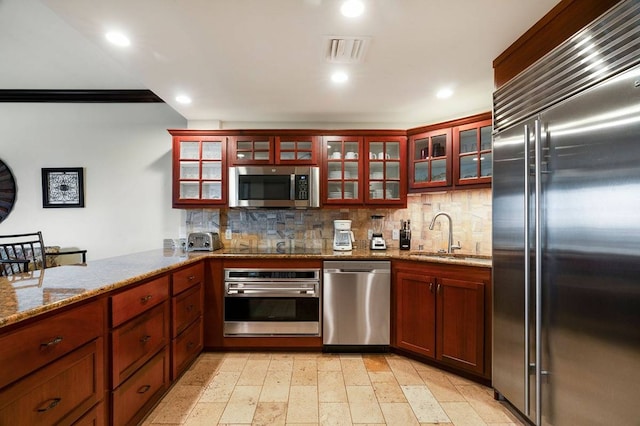 kitchen with light tile floors, light stone countertops, appliances with stainless steel finishes, backsplash, and sink