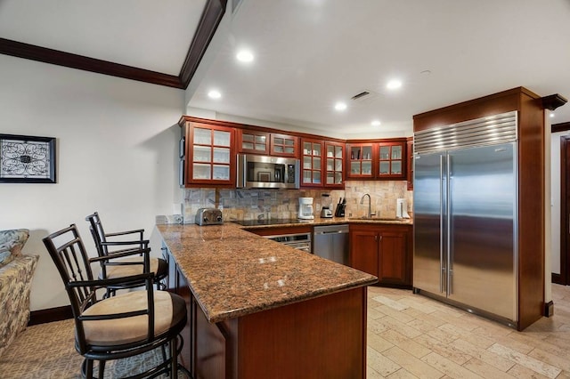 kitchen featuring stainless steel appliances, stone countertops, kitchen peninsula, a breakfast bar, and tasteful backsplash