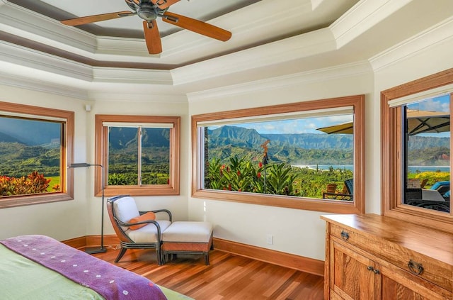 bedroom featuring dark wood-type flooring, a mountain view, ceiling fan, ornamental molding, and a tray ceiling