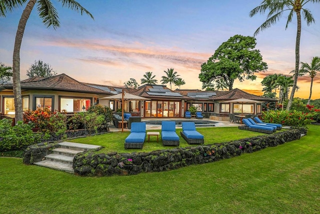 back house at dusk featuring a lawn and a patio area