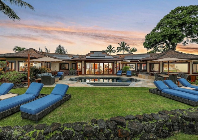 back house at dusk with outdoor lounge area, solar panels, a patio area, and a lawn