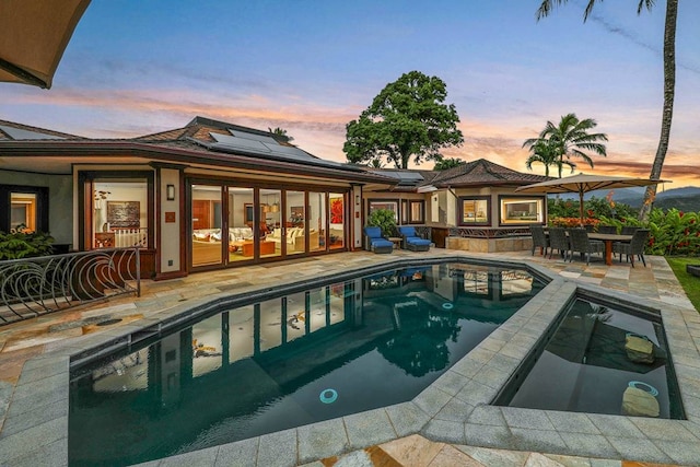 pool at dusk featuring an in ground hot tub and a patio