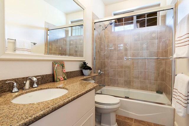 full bathroom featuring shower / bath combination with glass door, toilet, tile floors, and vanity with extensive cabinet space