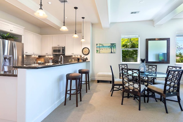 kitchen with light colored carpet, kitchen peninsula, appliances with stainless steel finishes, white cabinetry, and backsplash