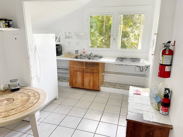 kitchen with white refrigerator, light tile floors, gas stovetop, sink, and vaulted ceiling