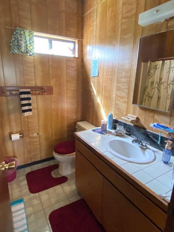 bathroom with toilet, vanity, and wood walls