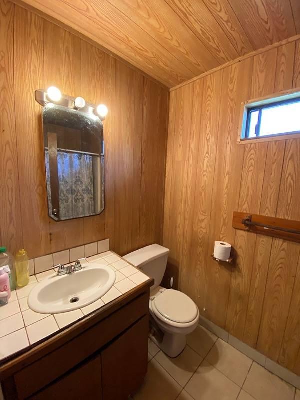 bathroom with toilet, vanity, tile patterned floors, wood walls, and wooden ceiling