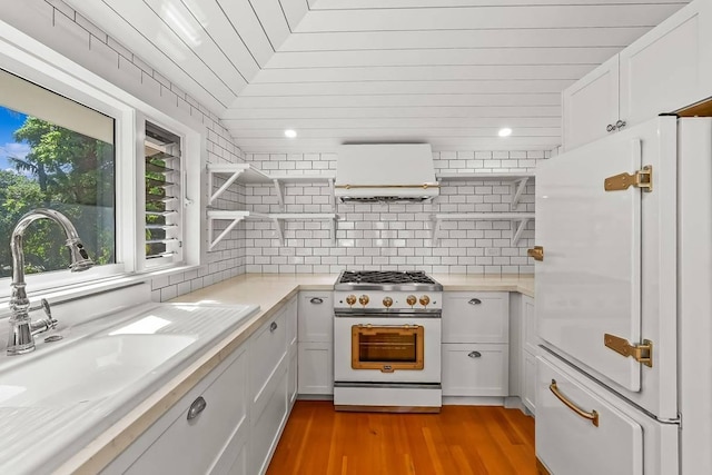 kitchen featuring light hardwood / wood-style floors, high end stove, sink, white cabinets, and white fridge