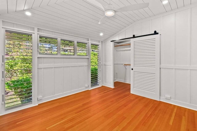 unfurnished bedroom featuring a barn door, light hardwood / wood-style flooring, wooden ceiling, and vaulted ceiling