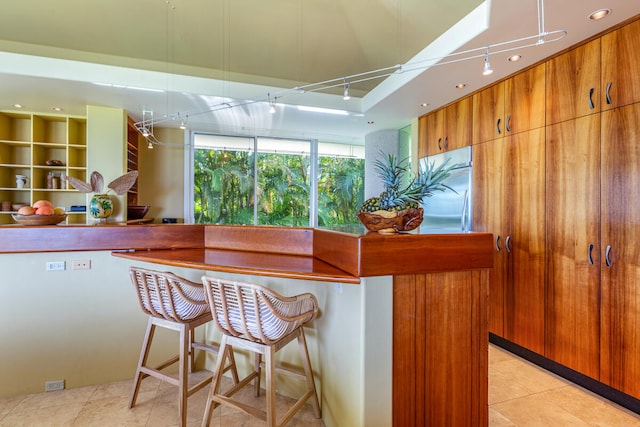 kitchen featuring rail lighting, a kitchen breakfast bar, stainless steel refrigerator, and light tile patterned floors