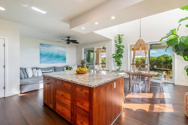 kitchen featuring a center island, hanging light fixtures, dark hardwood / wood-style floors, ceiling fan, and light stone countertops