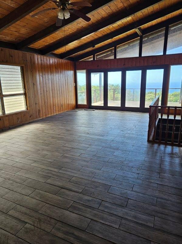 interior space with wood walls, lofted ceiling with beams, dark hardwood / wood-style floors, ceiling fan, and wood ceiling