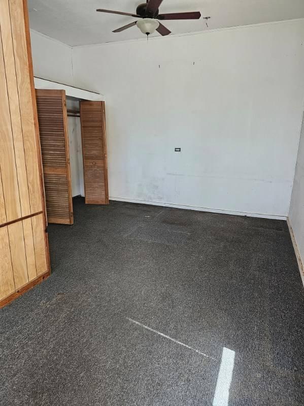 unfurnished room with ceiling fan and dark carpet